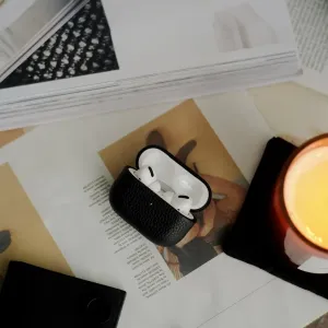 Juodas odinis KeyBudz AirPods Pro dėklas, atidarytas, su baltomis ausinėmis viduje, ant spausdintų puslapių
