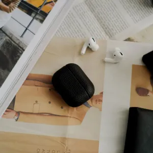 KeyBudz Artisan Series odinis dėklas, skirtas AirPods Pro 2, juodos spalvos, pavaizduotas ant žurnalo, šalia matomos baltos ausinės