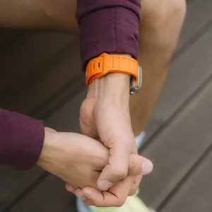 KeyBudz Journey oransje Apple Watch-rem på håndledd med grå urkasse i et utendørsmiljø.