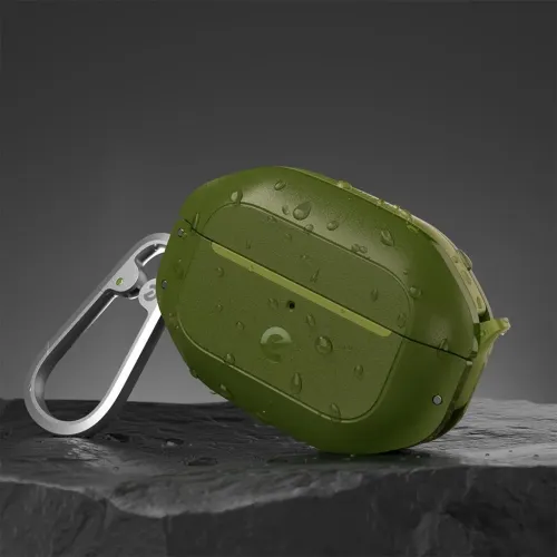 Skovgrønt AirPods Pro 2-etui med karabinhage, vanddråber på overfladen, LED-huller og hængsler foran, lænet op ad en mørk stenbase.