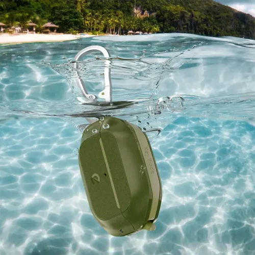 Skovgrønt AirPods Pro-etui med sølvfarvet karabinhage ses delvist under vandet med strand og palmer i baggrunden.