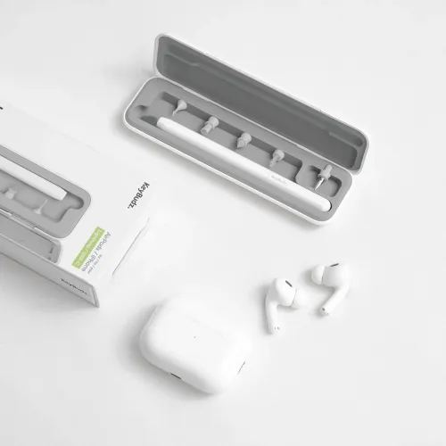 AirCare 2.0-rengøringssæt i åbent etui med udskiftelige spidser, ved siden af emballage, AirPods-etui og to ørepropper.