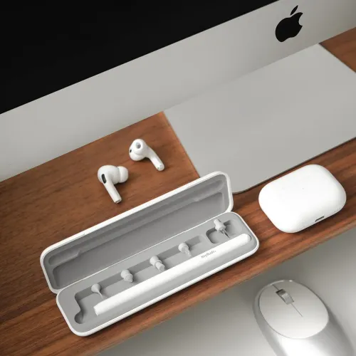 KeyBudz AirCare 2.0-rengøringssæt i åbent etui med flere spidser og rengøringspen, på træbord ved siden af AirPods og etui.