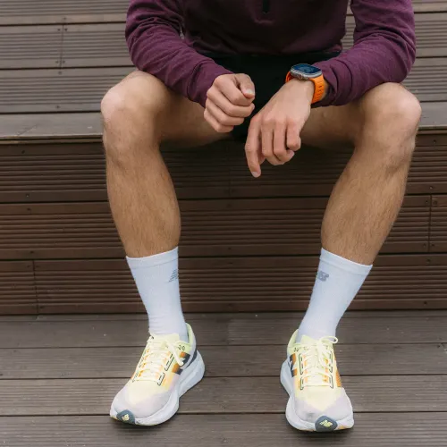 Elektrisk oransje Apple Watch-armbånd med riflet design på håndleddet; klokken bæres av en sittende person på en tretrapp.